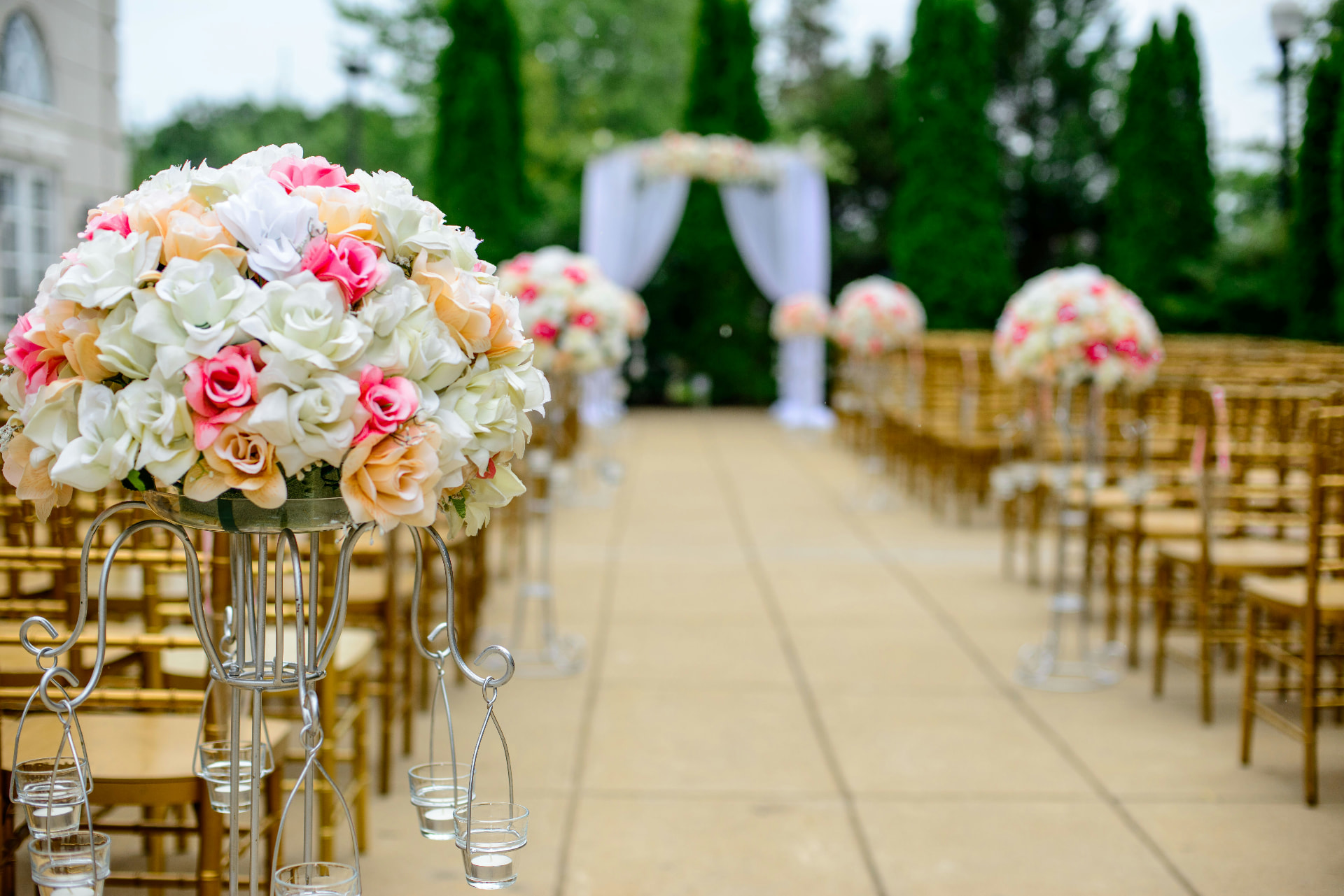 Outdoor wedding aisle lined with blush and ivory floral arrangements